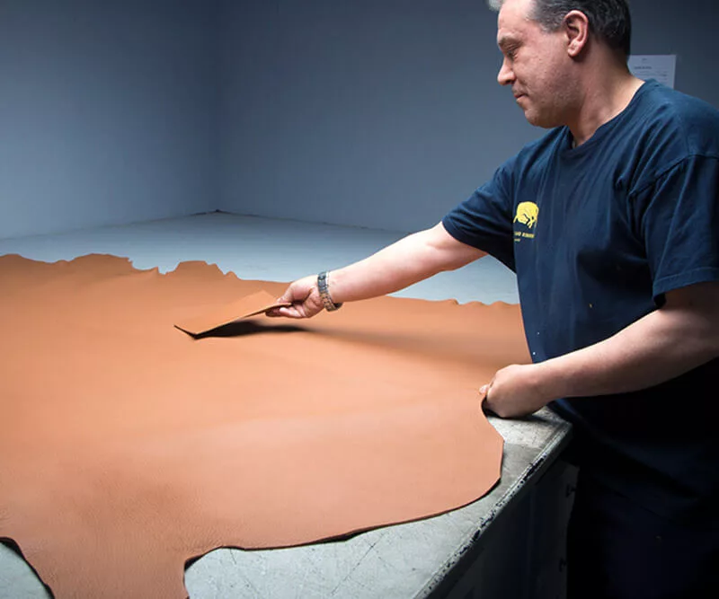 Artisan manipulant une grande pièce de cuir sur une table de travail.