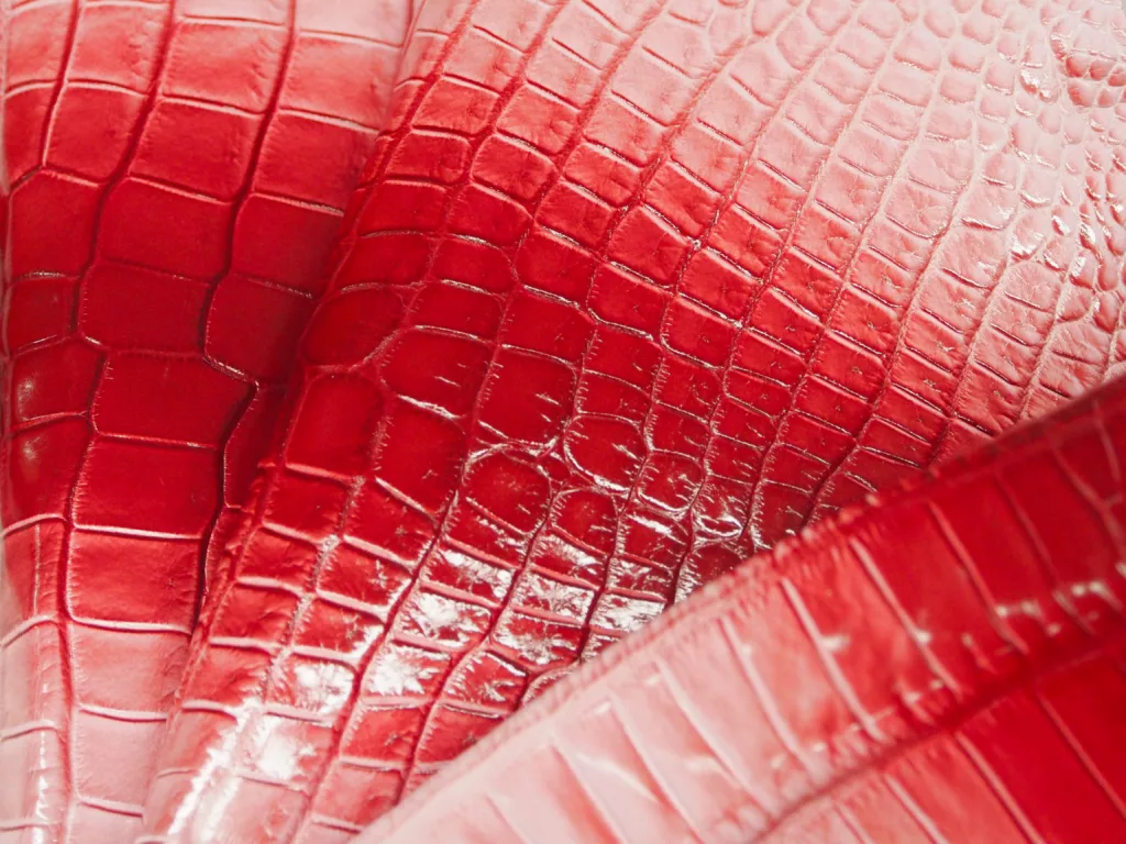 Elegant, bright red crocodile leather with a subtle gradation from dark red to pale pink. The scaly texture is visibly detailed, highlighting the leather's exceptional quality.