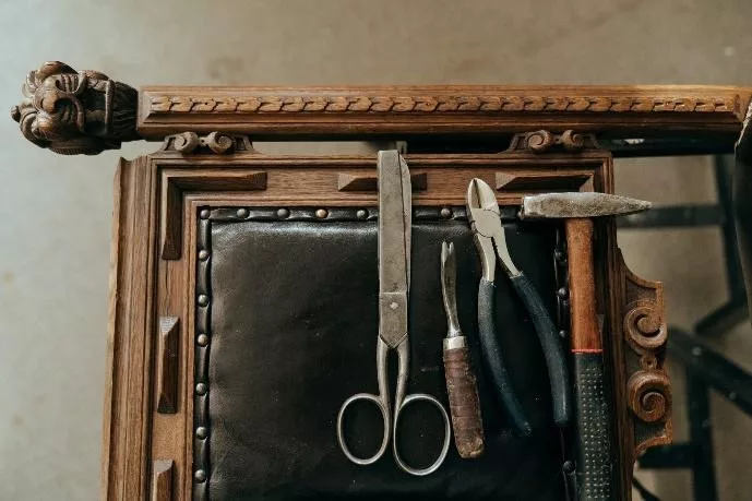 Leatherworking tools arranged on a piece of dark leather, resting on a carved wooden frame.