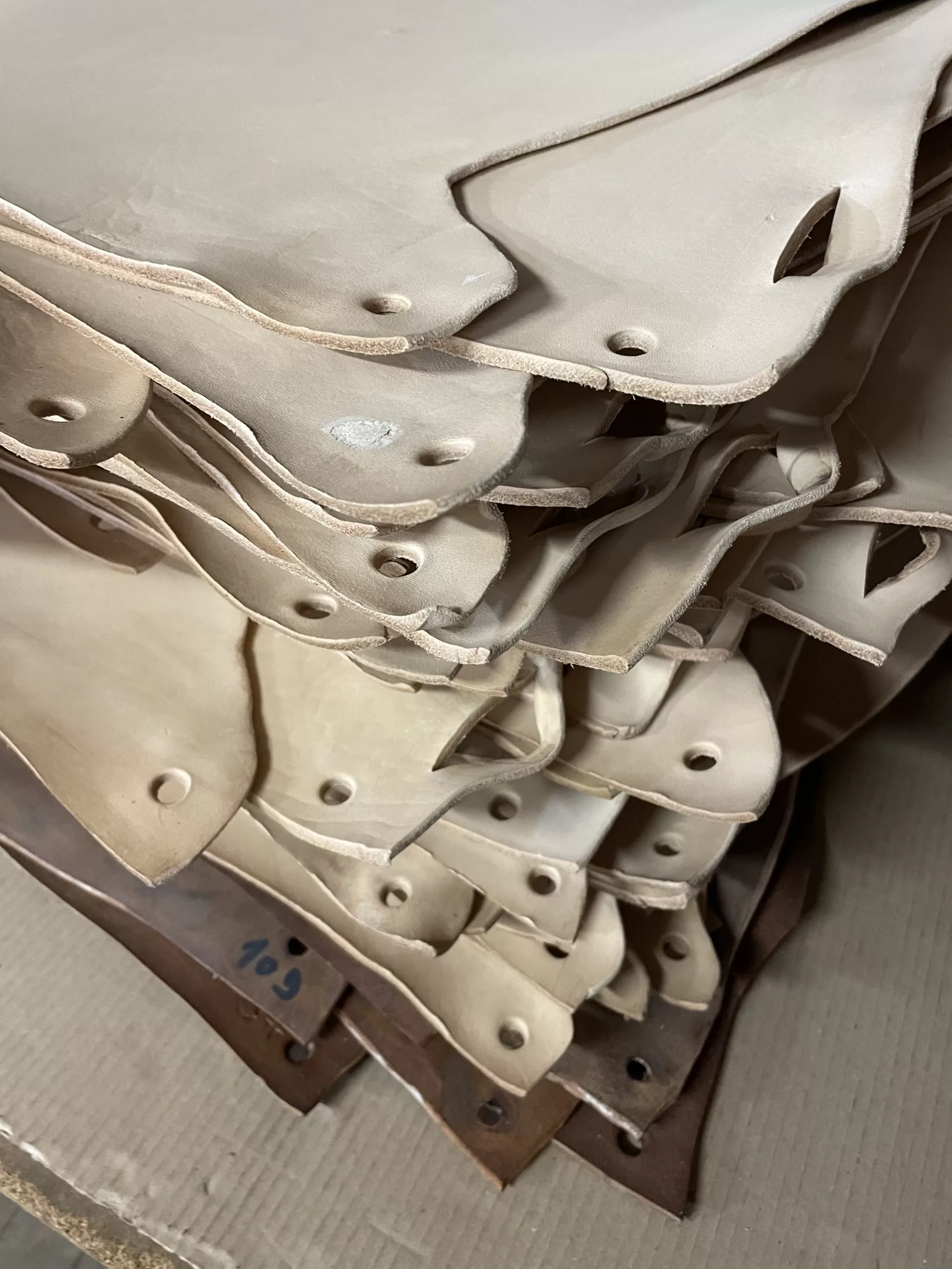 Stack of beige cowhide pieces with irregular edges and punched holes, ready for further use.