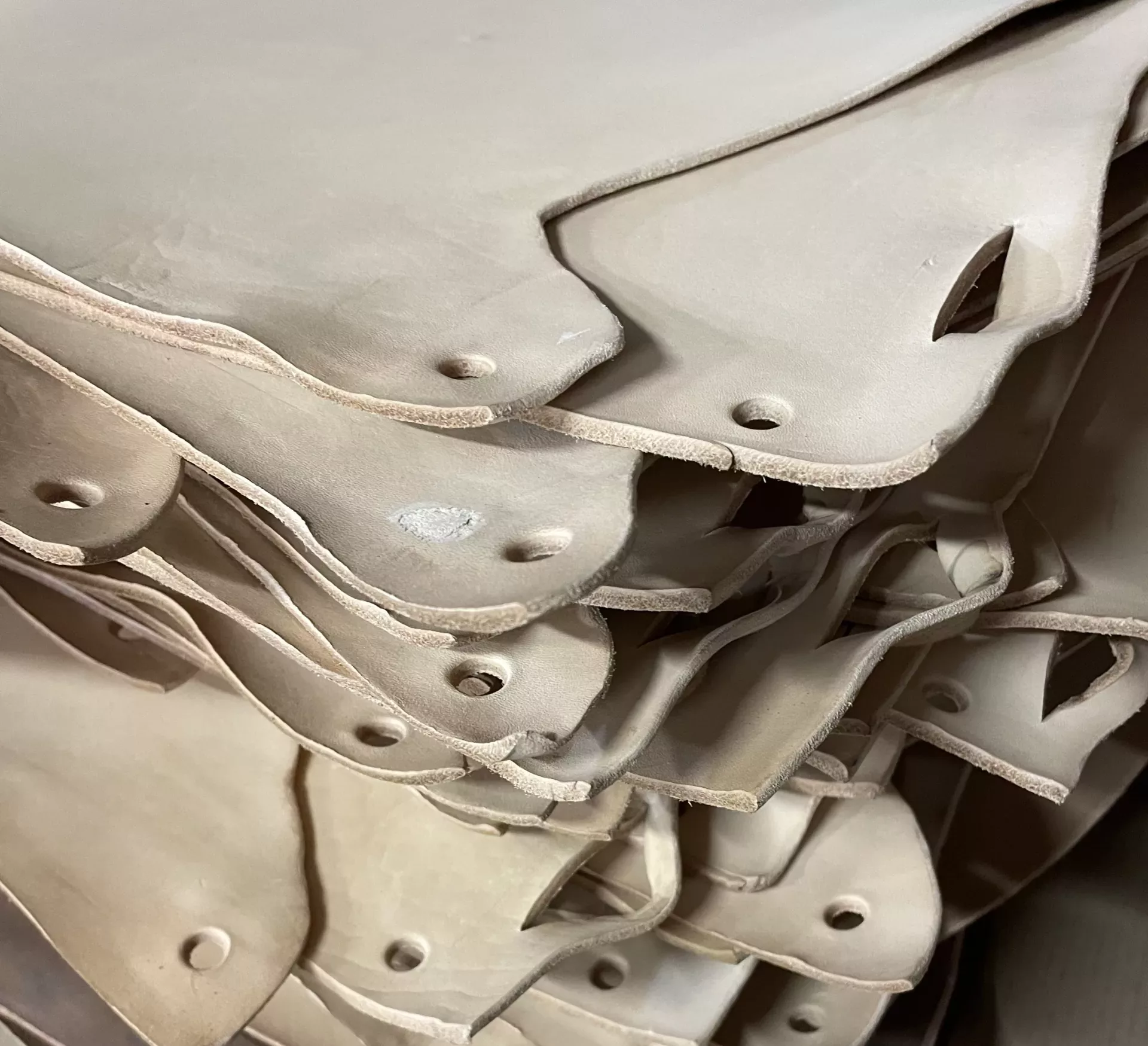 Pezzi di pelle bovina sospesi a barre di legno, disposti in file e di colore beige, in fase di essiccazione.