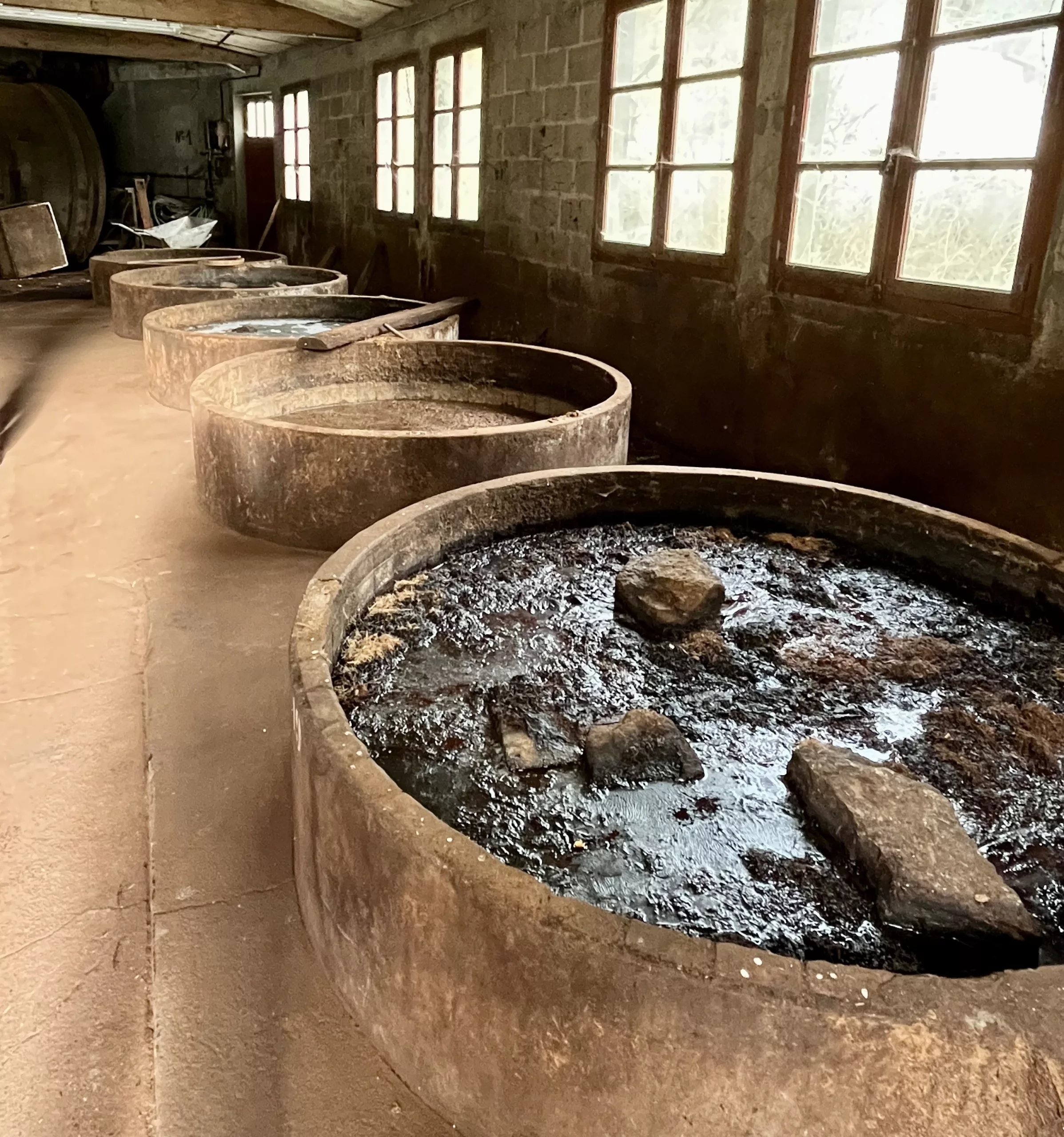 Vegetable tanning pits with vats filled with dark brown liquid, wood pieces, and stones, used for tanning leather with oak bark.