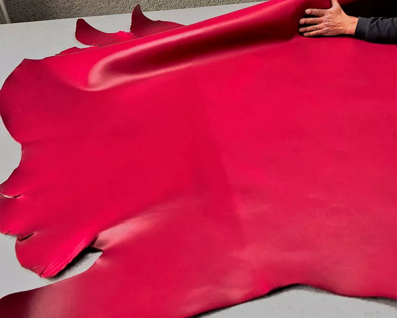 Cuir de veau rouge manipulé à la main sur une surface de travail.